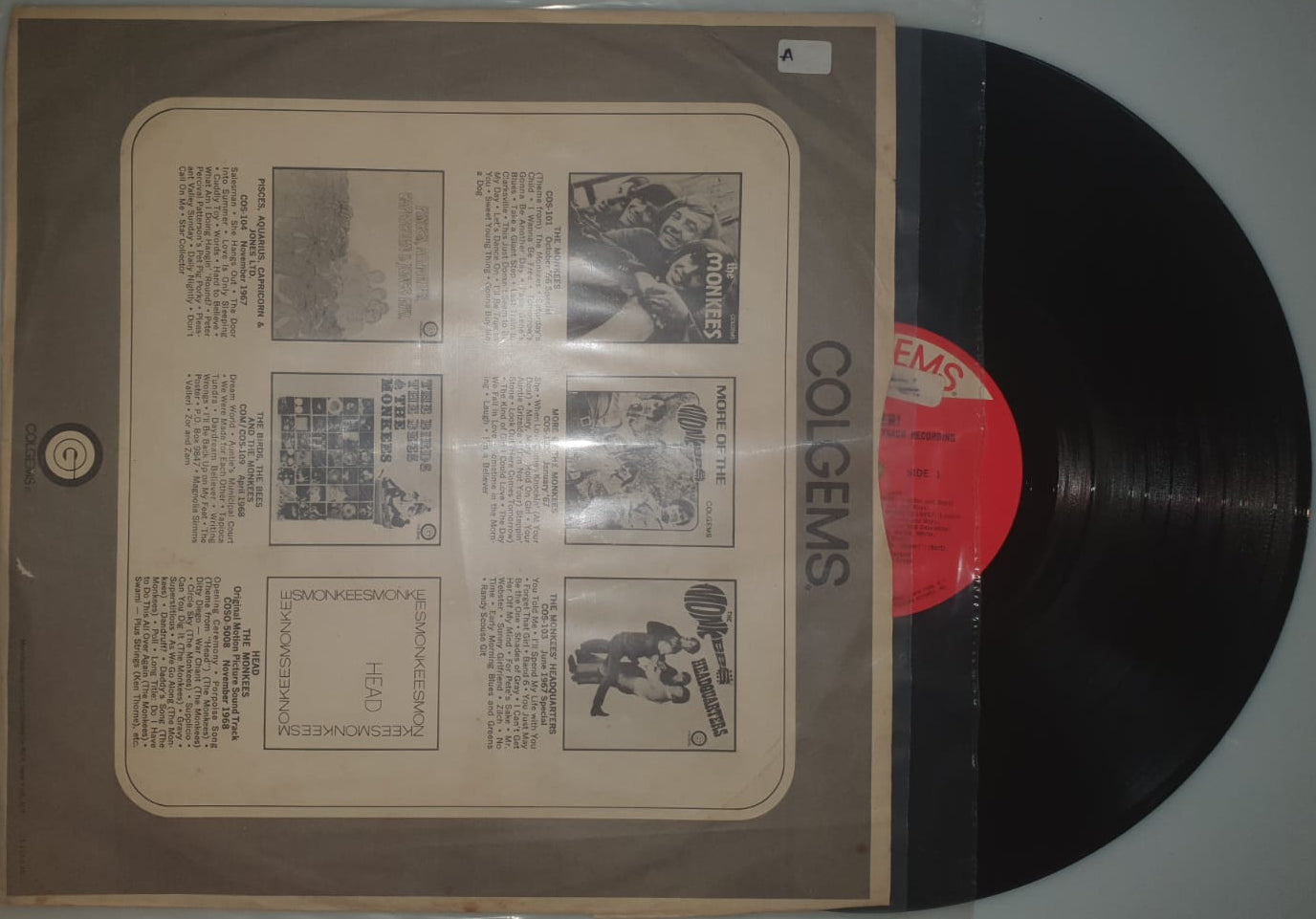Vinyl record with a red label and a brown paper sleeve on a gray wall.